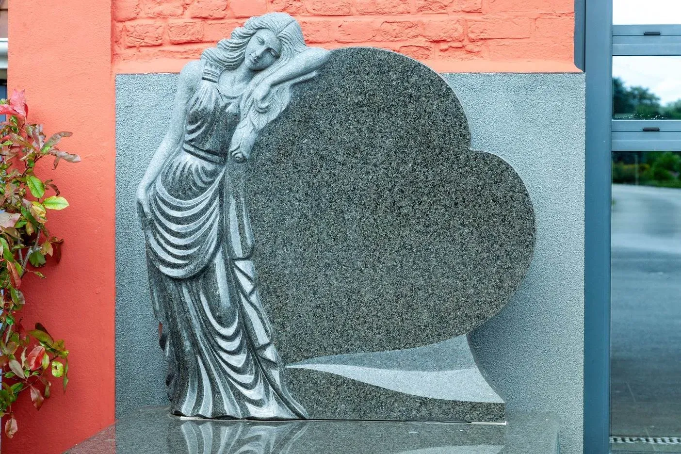 Stèle en granit sculptée représentant une figure féminine appuyée sur un cœur.